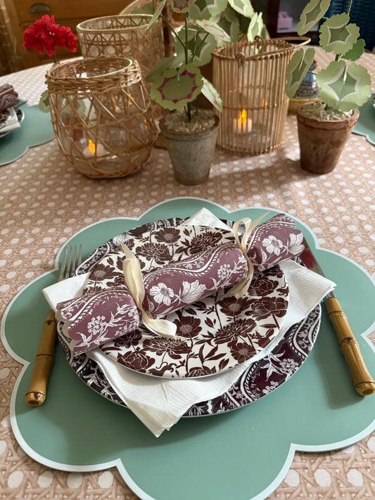 Domino Oxblood party cracker on a matching oxblood and white patterned plate, set on a sage scalloped placemat with bamboo flatware and candle lanterns behind