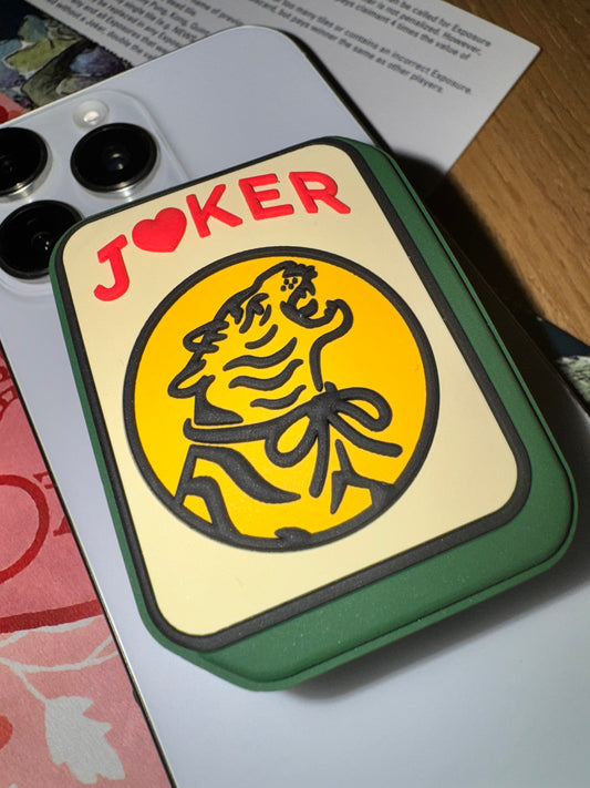 Close-up of the Joker phone grip showing the roaring tiger in a yellow circle on a cream tile face with a green edge