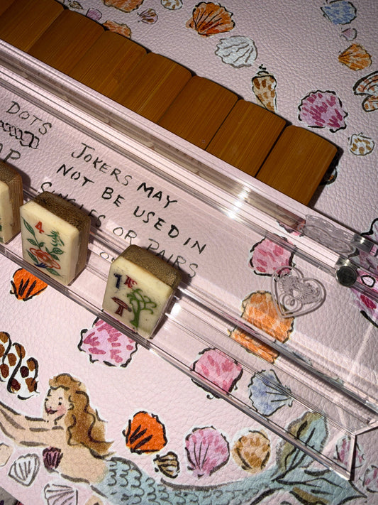 Clear acrylic logo rack holding tiles on a seashell and mermaid print mahjong mat