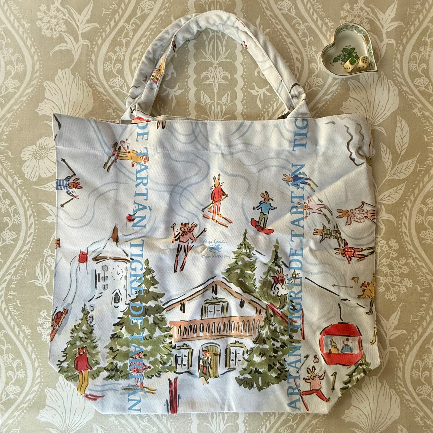 Après Mahj jumbo slouchy denim tote laid flat, showing the alpine lodge, skiers, chairlift and pine trees