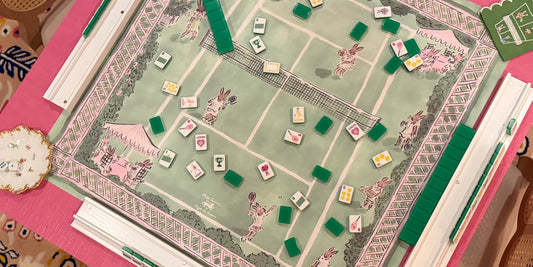 The Paige Spearin Bunny Love mahjong mat mid-game — an illustrated tennis court of bunnies in pink and green, tiles and racks in play on a hot pink table