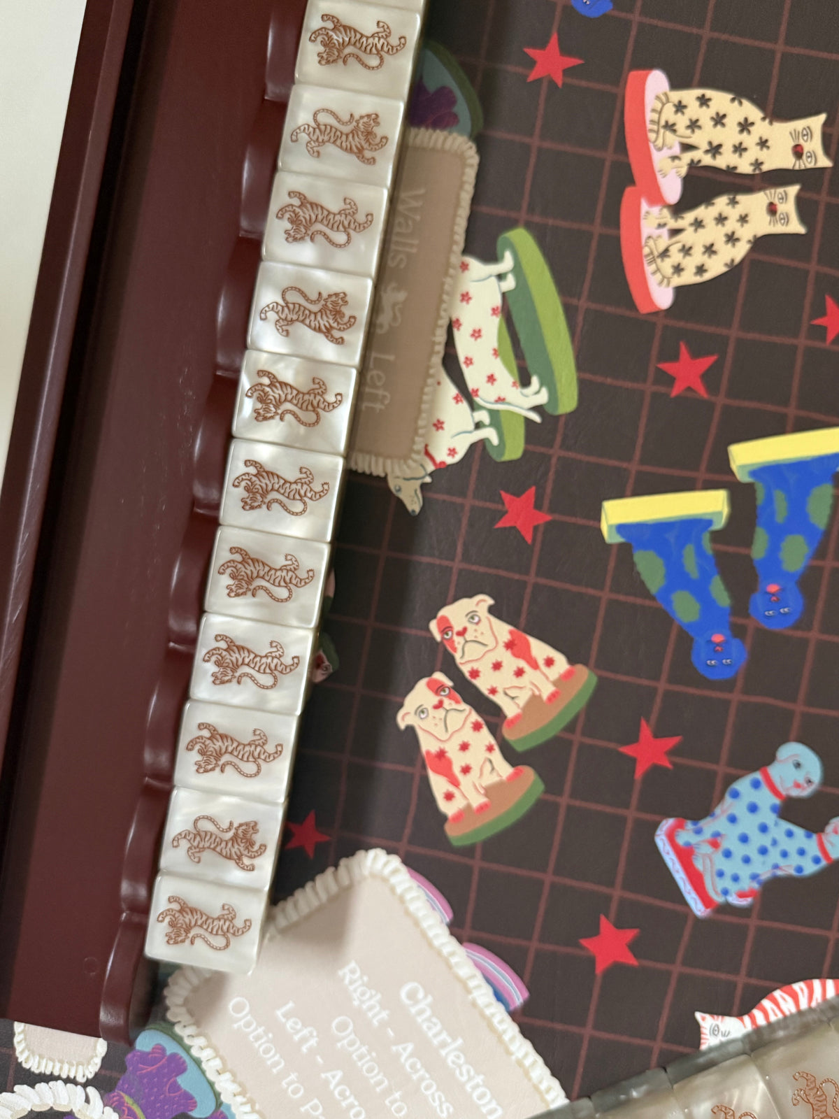 Row of cream tiger-back tiles lined up in an oxblood mahjong rack, resting on a mahjong rules card