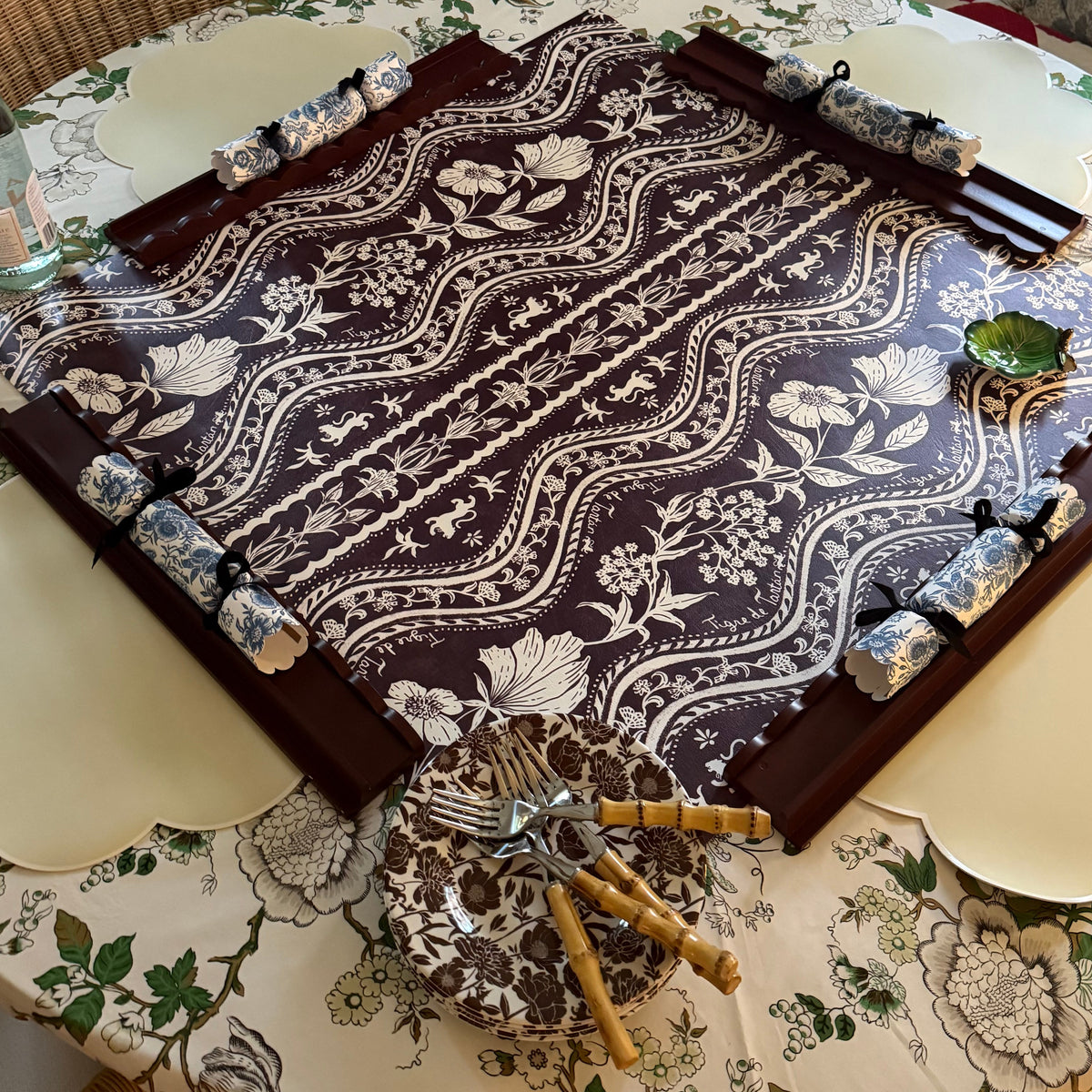 Domino Oxblood party crackers laid along the edges of a Domino Oxblood mahjong mat on a table set with floral plates