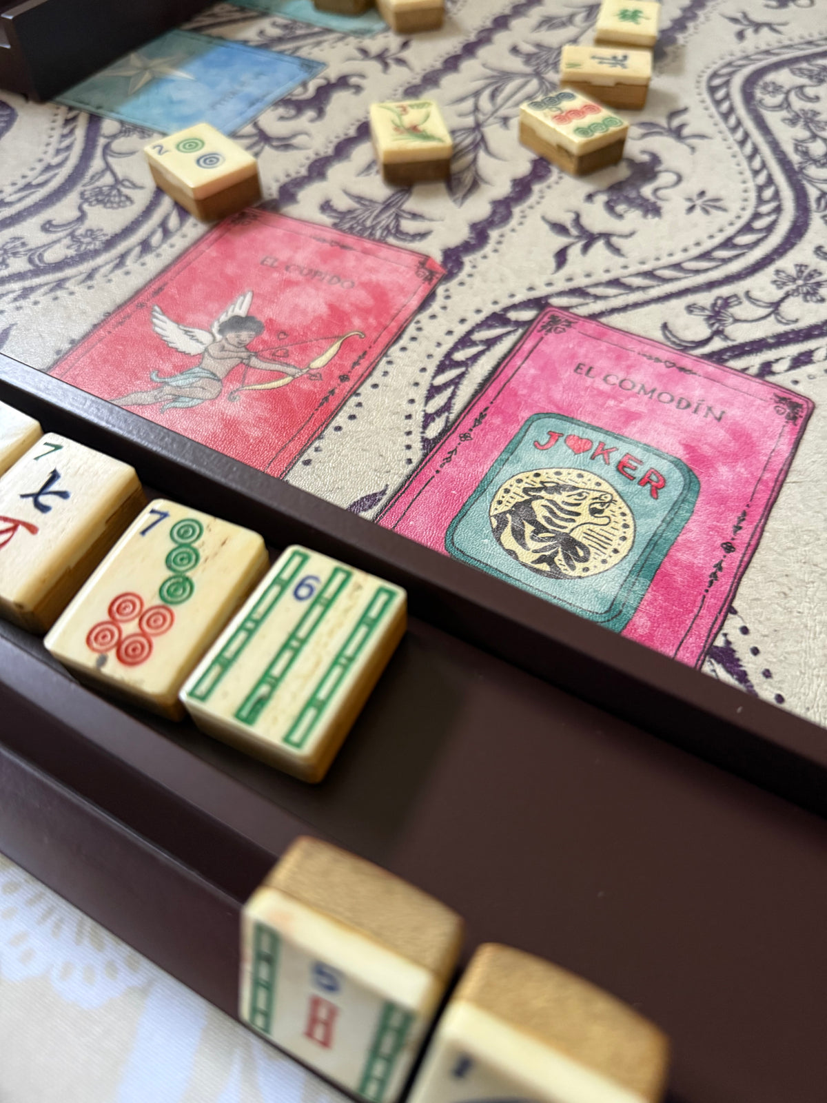 Rich raisin rack holding bamboo-back tiles beside pink card prints on a mahjong mat