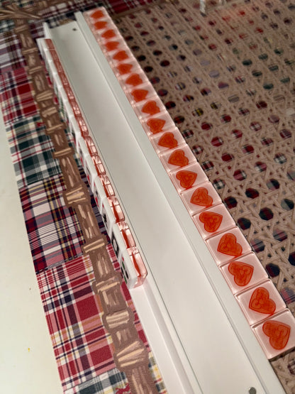 Row of red heart tiles lined up in a white mahjong rack on a cane-pattern mat