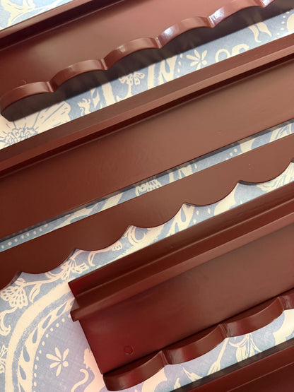 Empty oxblood wooden mahjong racks with scalloped pushers stacked together, showing the wavy scalloped edge