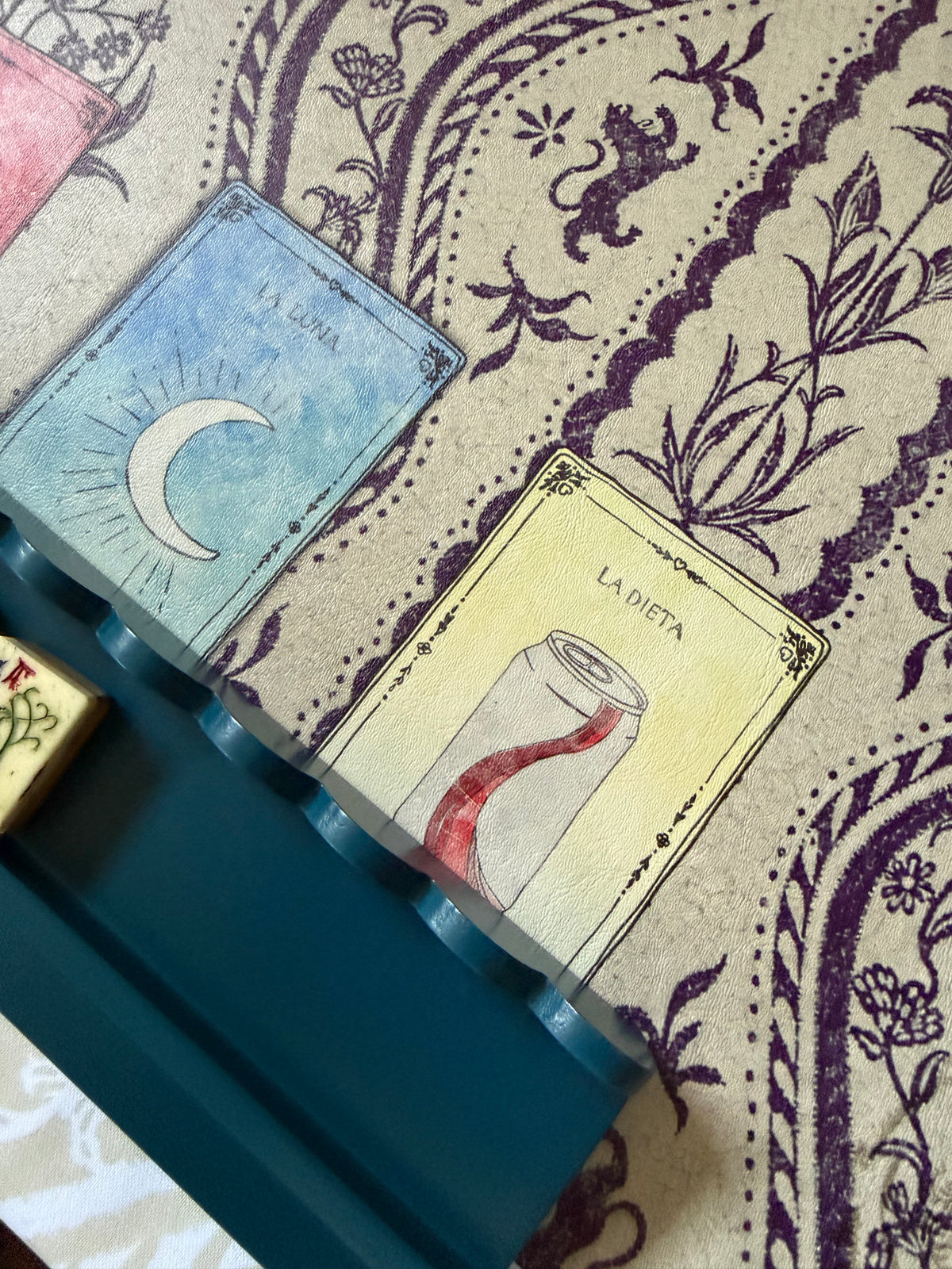 Close-up of a marine blue scalloped rack edge on a purple paisley mat with card illustrations