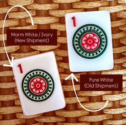 Close comparison of two one-dot mahjong tile faces, the new warm white and ivory shipment beside the older pure white shipment, showing the difference in tile color.