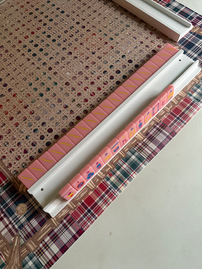 White mahjong rack with pink and coral tiles on a cane-pattern mat with plaid edge