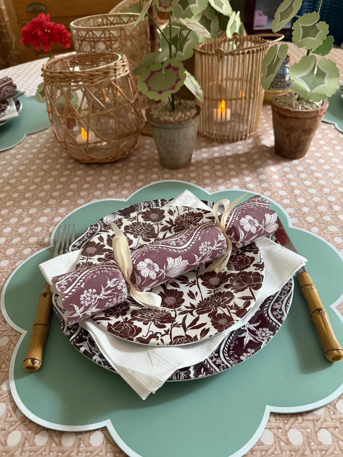 Domino Oxblood party cracker on a matching oxblood and white patterned plate, set on a sage scalloped placemat with bamboo flatware and candle lanterns behind