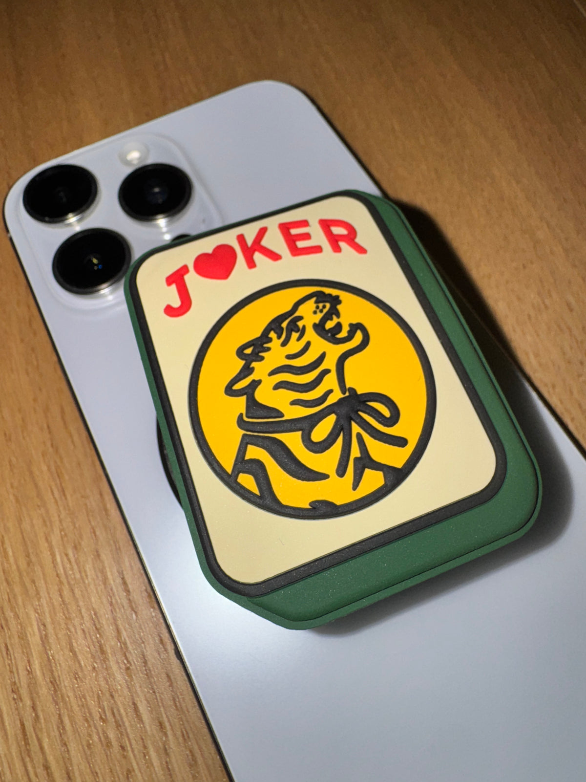 Joker phone grip attached to a silver iPhone lying on a wooden table