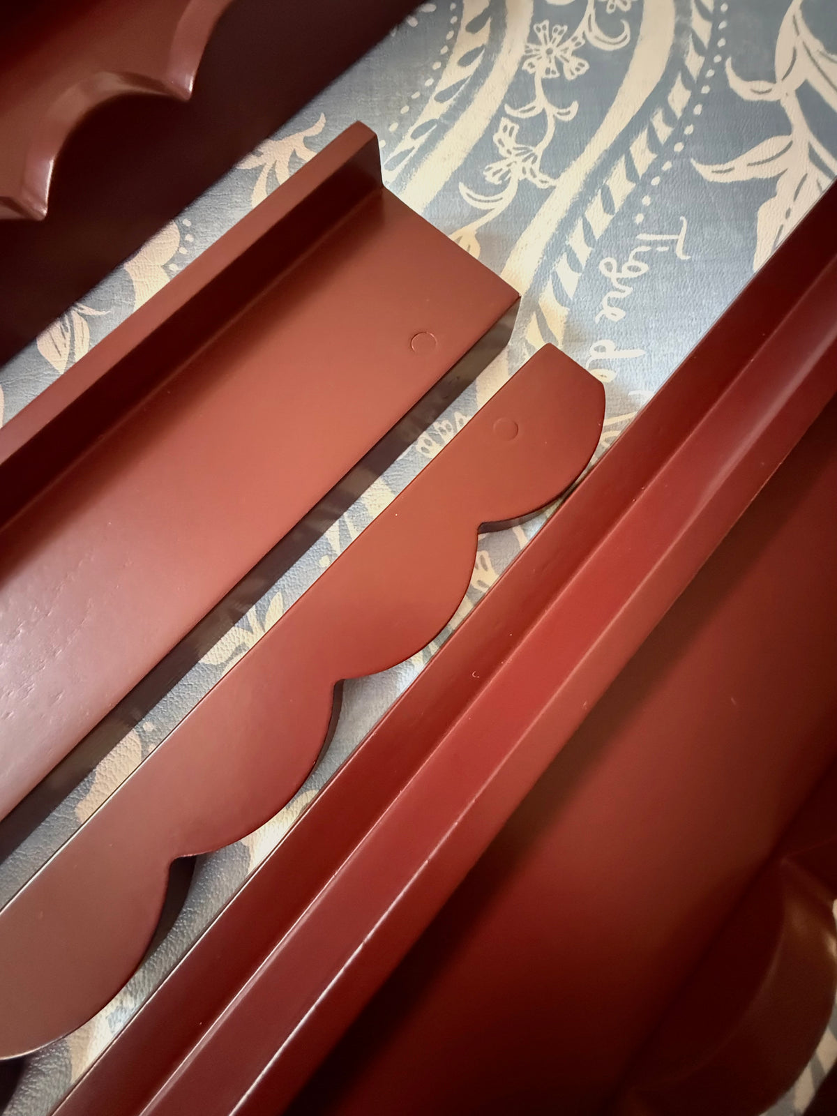 Detachable scalloped pusher lifted away from an oxblood mahjong rack, showing the magnet points on both pieces