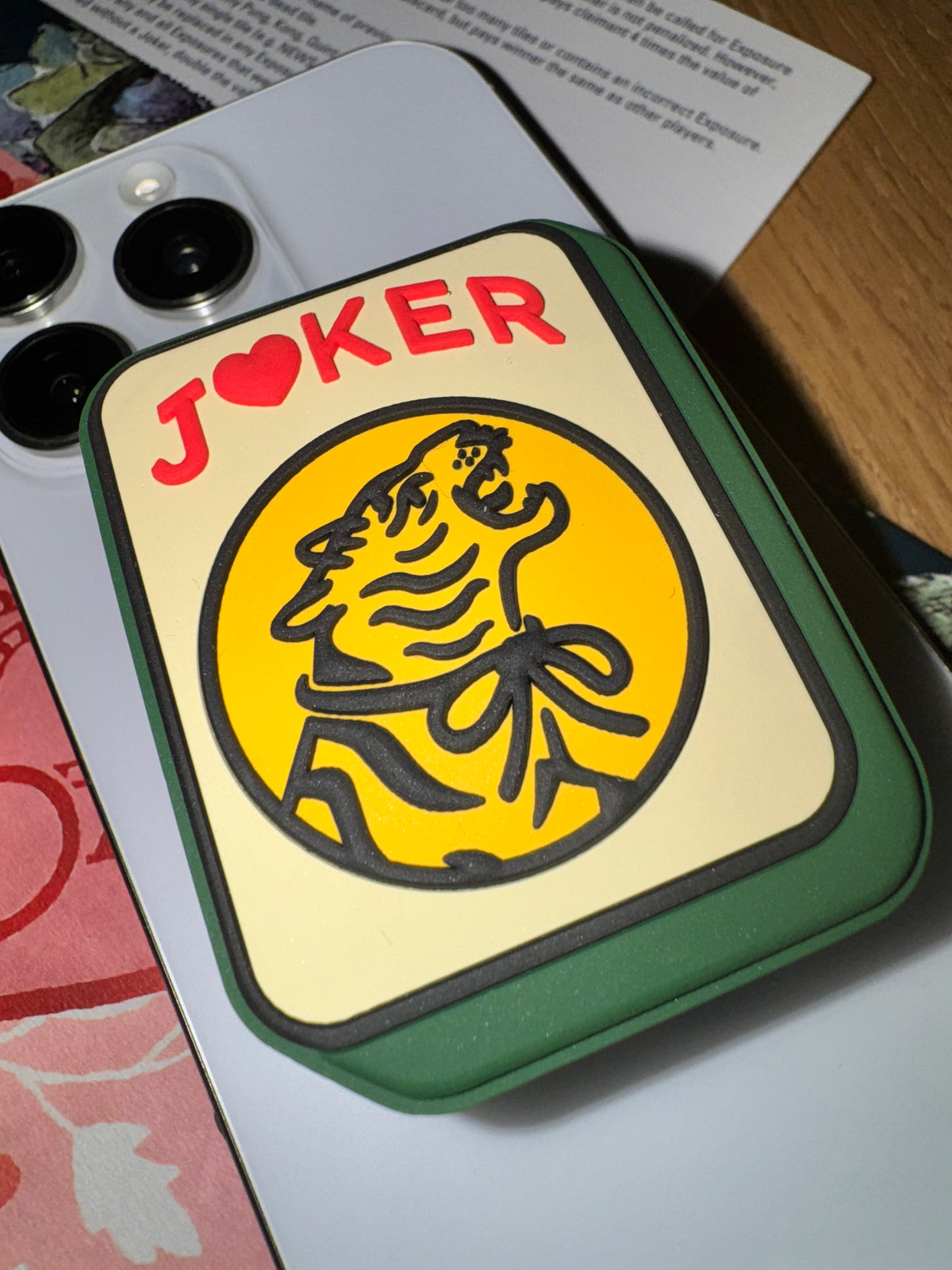 Close-up of the Joker phone grip showing the roaring tiger in a yellow circle on a cream tile face with a green edge