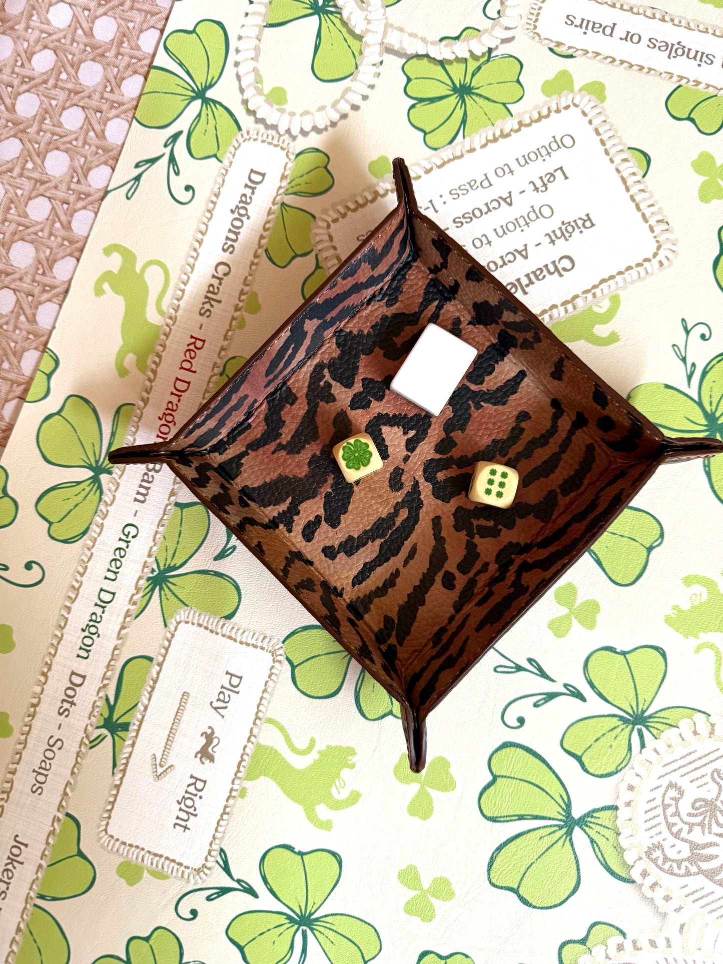 El Tigre tiger-stripe leather snap tray holding dice, styled on a clover-print mahjong mat