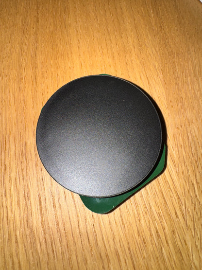 Back of the phone grip: black round magnetic base with green edge, on a wooden table