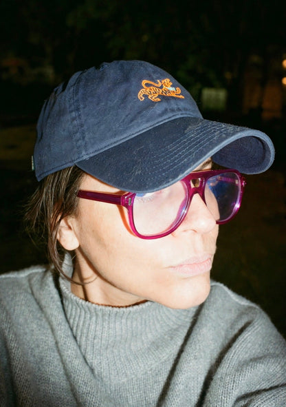 Woman in pink glasses wearing the navy logo cap with an orange embroidered tiger