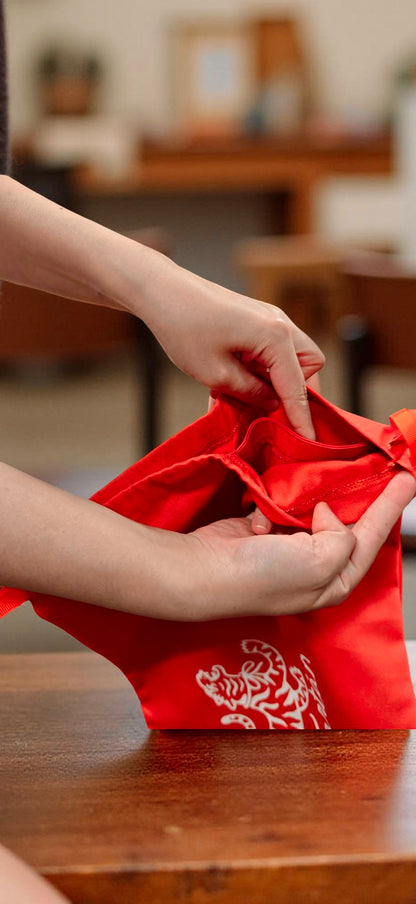 Hands opening a red cotton twill dust bag with white tiger logo
