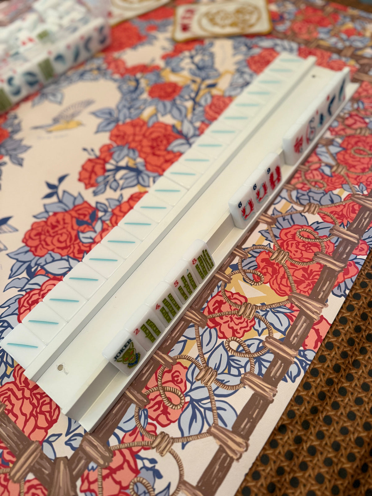 White mahjong rack holding colorful tiles on a red and blue floral mahjong mat