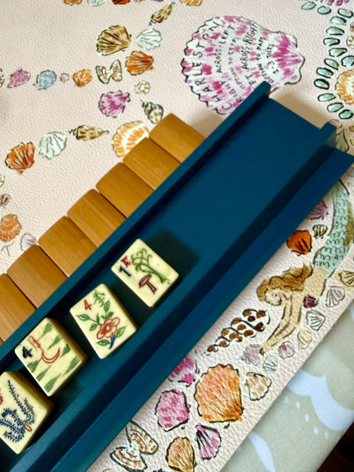 Marine blue straight rack holding bamboo-back tiles on a seashell-print mahjong mat