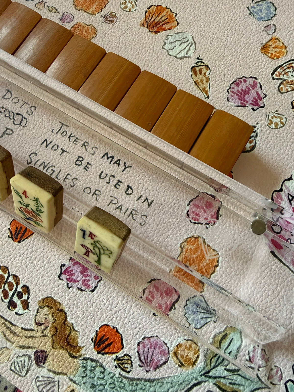 Clear acrylic logo rack with wooden and cream tiles on a seashell and mermaid print mat