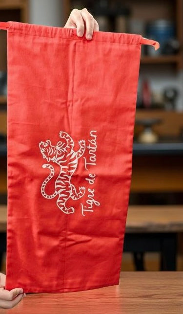 Red cotton twill dust bag with white Tigre de Tartán tiger logo, held upright