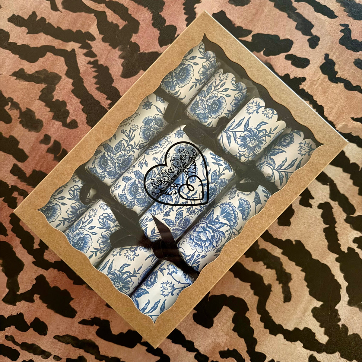 Set of four Chinoiserie Bleu party crackers in a kraft gift box with a window lid, sealed with a heart-shaped Tigre de Tartán sticker, on a tiger-stripe surface