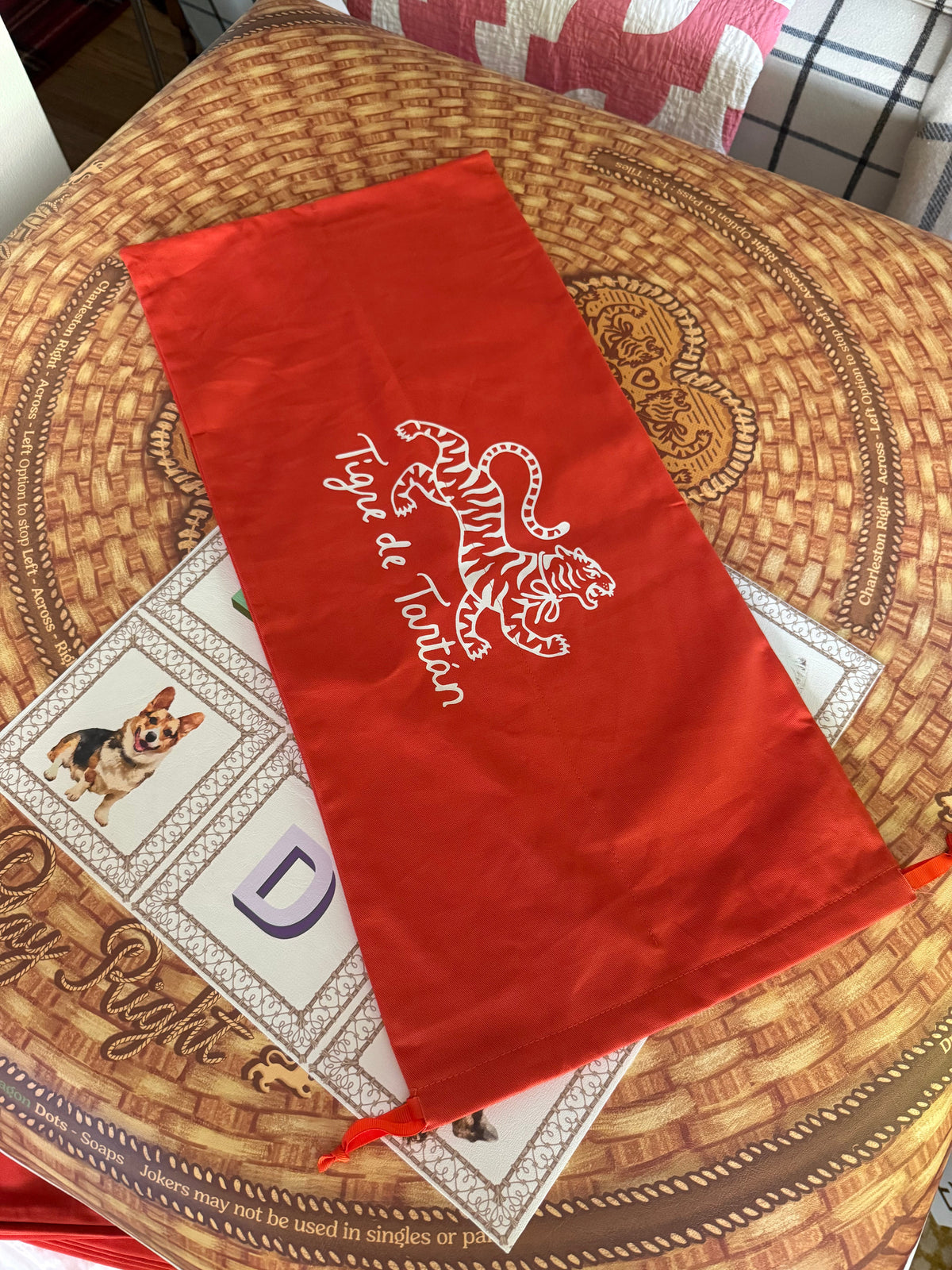 Red cotton twill storage bag with white Tigre de Tartán tiger logo on a basket-print mahjong mat