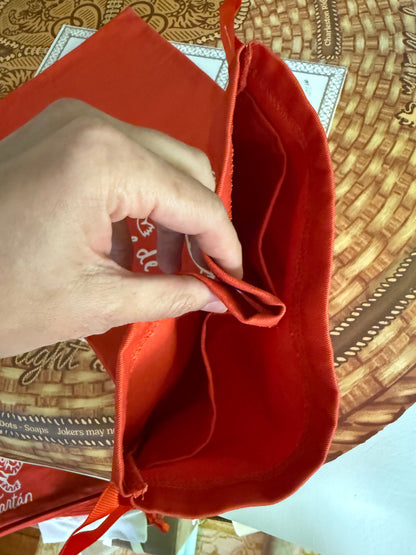 Hand opening a red cotton twill rack storage bag to show the interior compartments