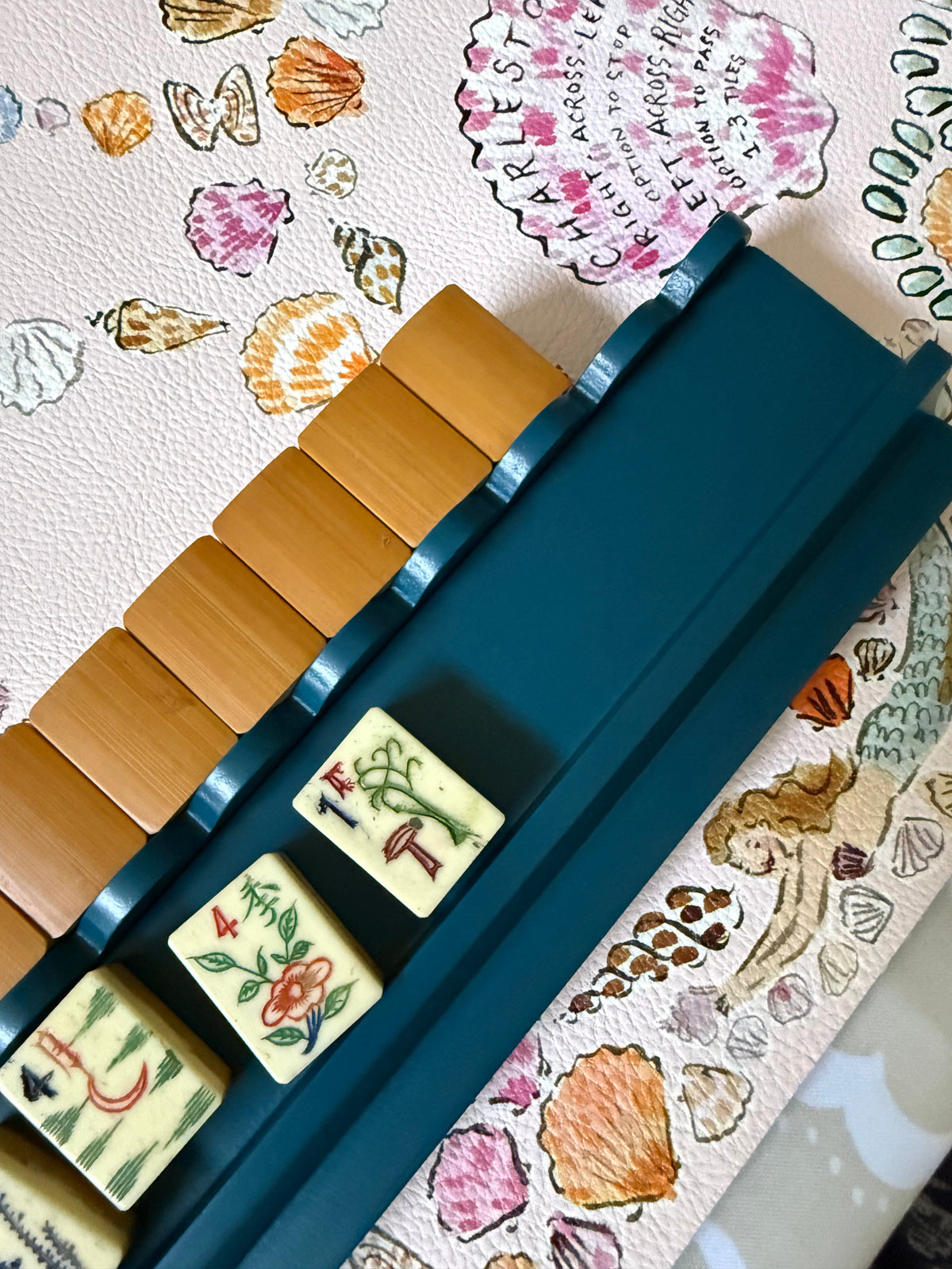 Marine blue scalloped rack holding bamboo-back tiles on a seashell-print mahjong mat