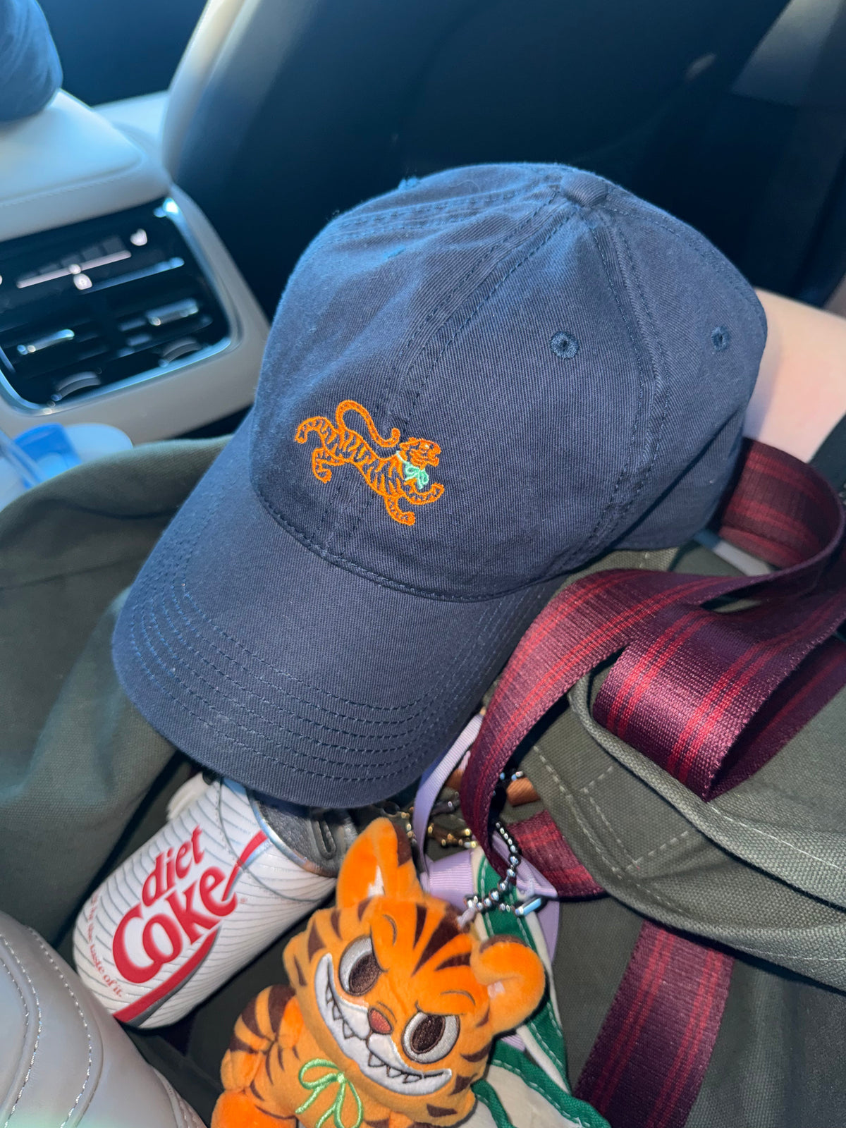Navy logo cap with an orange embroidered tiger, resting on a bag beside a tiger keychain