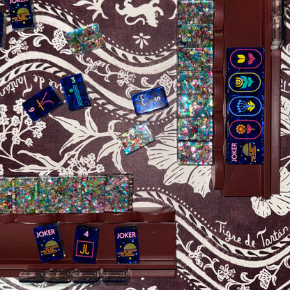 Oxblood wooden mahjong racks holding a set of glittery navy and confetti tiles on a Tigre de Tartán tartan tablecloth