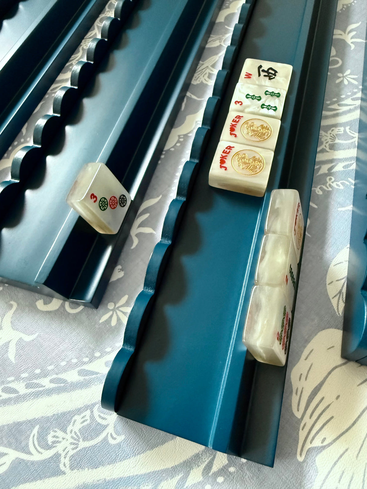 Marine blue scalloped mahjong racks holding cream tiles on a blue and cream floral fabric