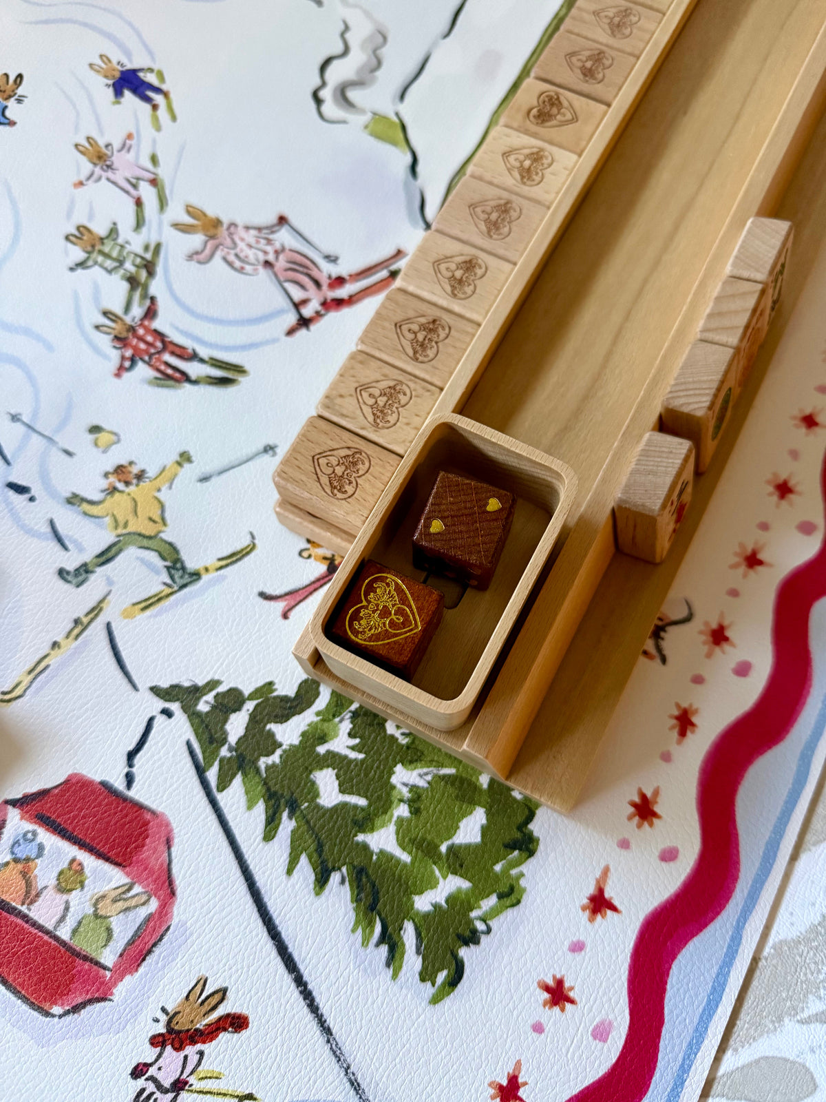 Two brown wooden logo dice in a rack tray on the Paige Spearin Après Mahj alpine mahjong mat