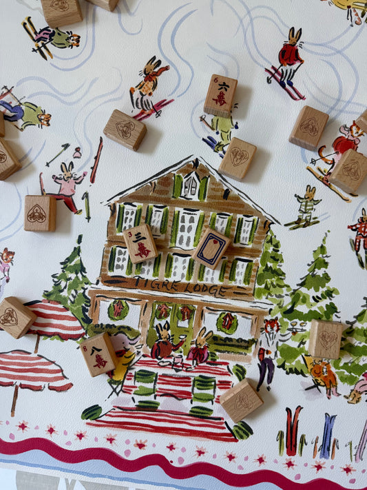 Paige Spearin Après Mahj mahjong mat: hand-illustrated Tigre Lodge ski chalet with skiing rabbits and tigers, wooden mahjong tiles scattered across the mat
