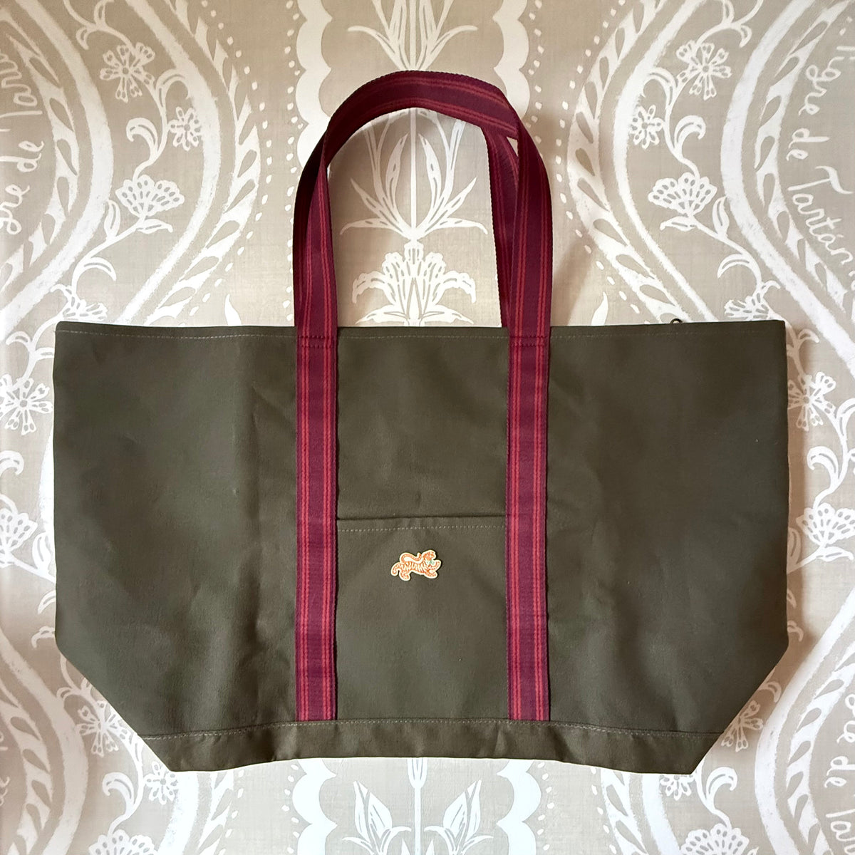 Signature XL Canvas Tote in olive canvas with burgundy striped handles, front pocket and small embroidered tiger patch, laid flat
