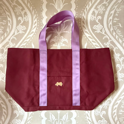 Signature XL Canvas Tote in oxblood canvas with lavender handles, front pocket and small embroidered tiger patch, laid flat