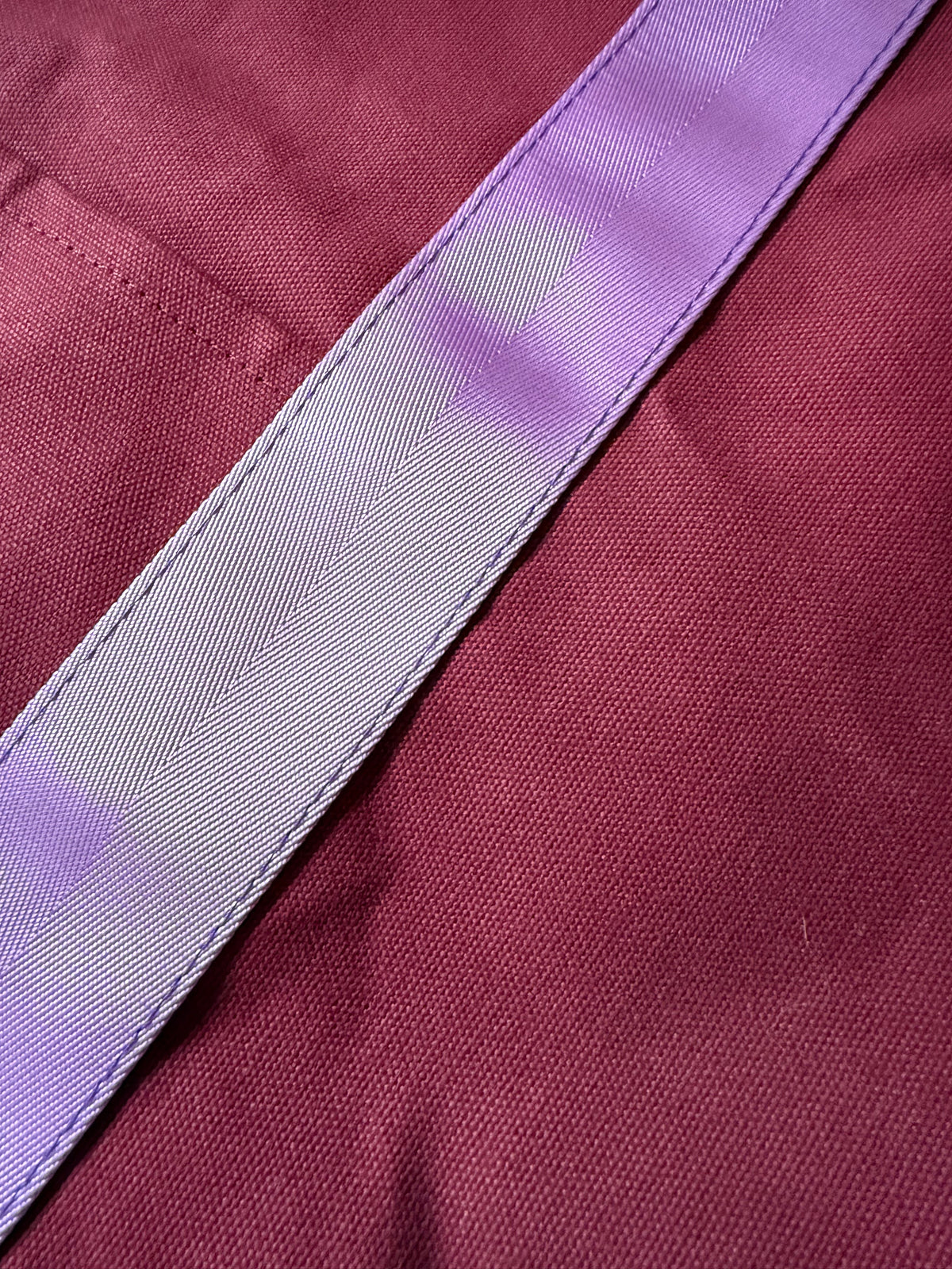 Close-up of a lavender webbing handle stitched to oxblood canvas