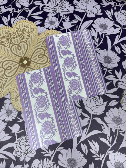 Two lavender and white Thorn-print mahjong tile shufflers beside a tan heart-motif accessory on a navy and lilac floral print