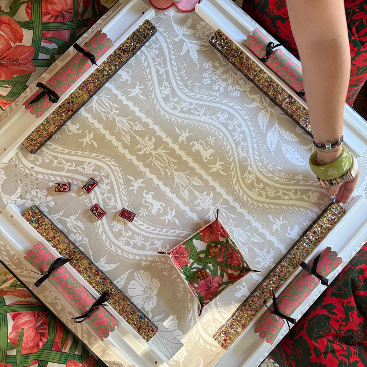 Domino Blonde rules-edition mahjong mat on a card table from above, with four beaded racks, red dice and a bowl of snacks
