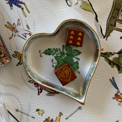 Two brown wooden logo dice in a heart-shaped porcelain dish on the Paige Spearin Après Mahj mahjong mat