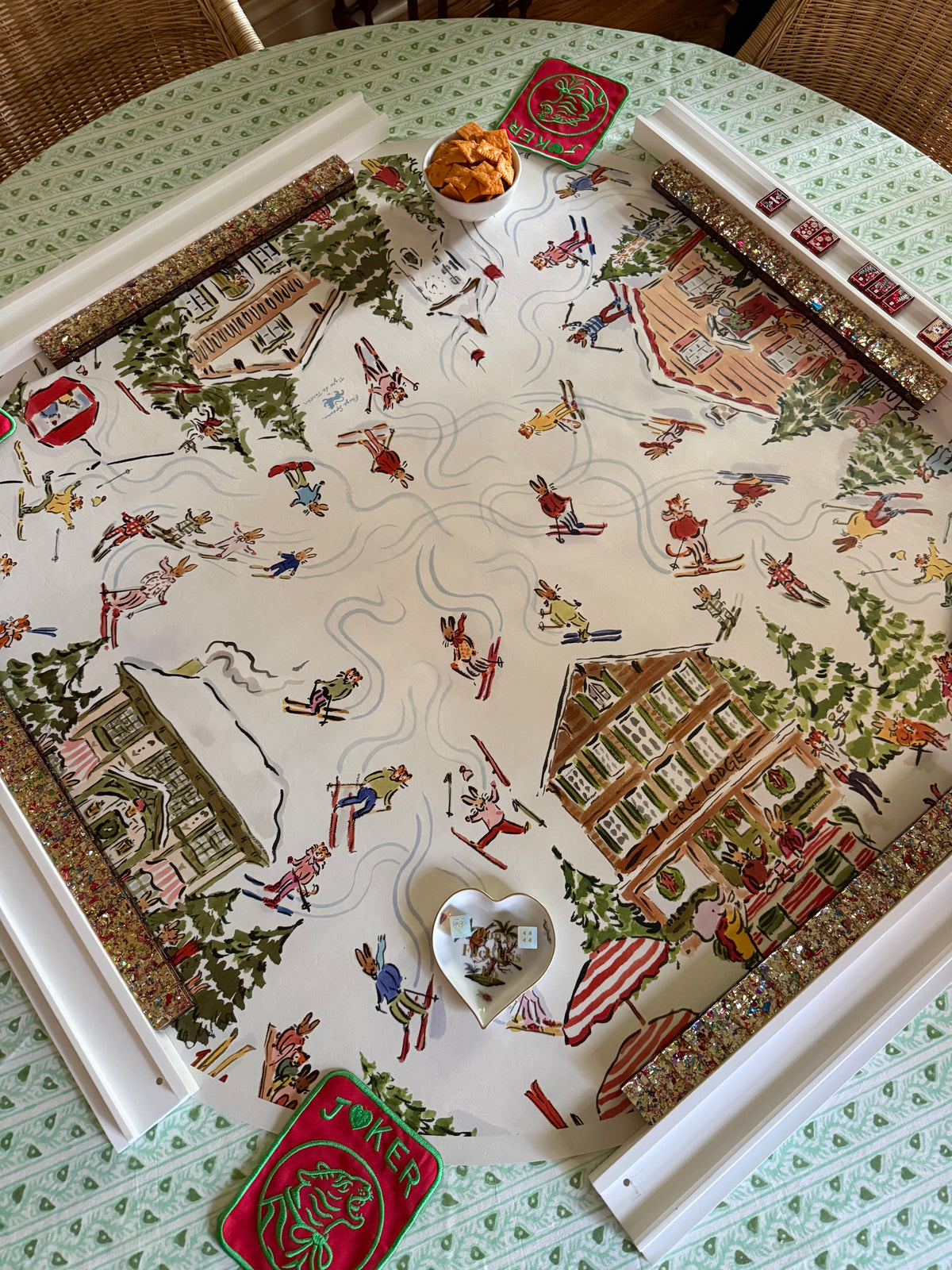 Après Mahj alpine village mahjong mat set on a round table with beaded racks, a heart-shaped dish and a red tin, from above