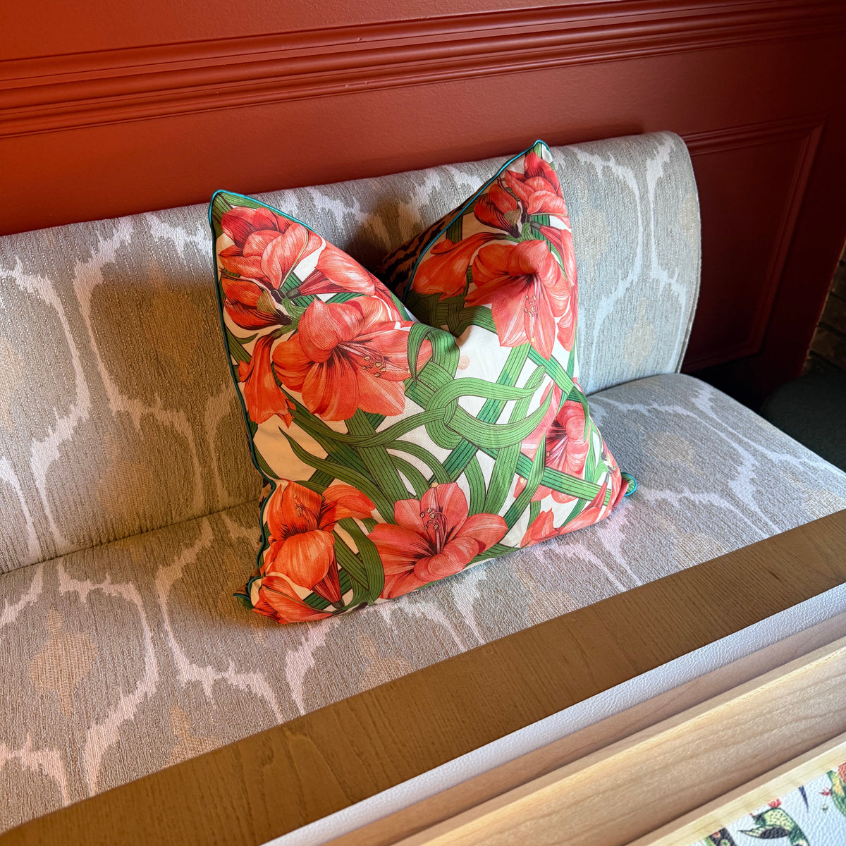 Estate Sale premium linen pillow in the red amaryllis trellis print on a grey patterned banquette against a red wall