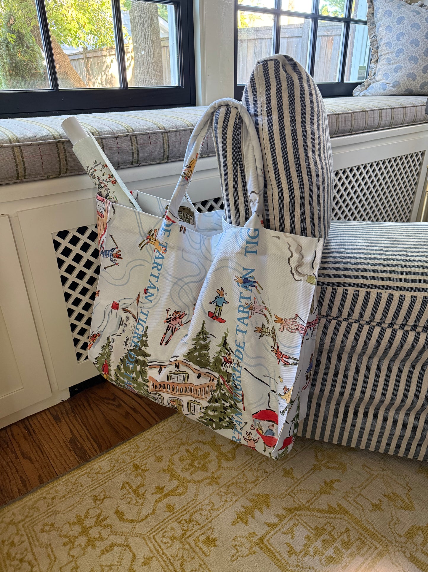Après Mahj jumbo slouchy denim tote hanging from a striped window-seat bench in a sunlit room