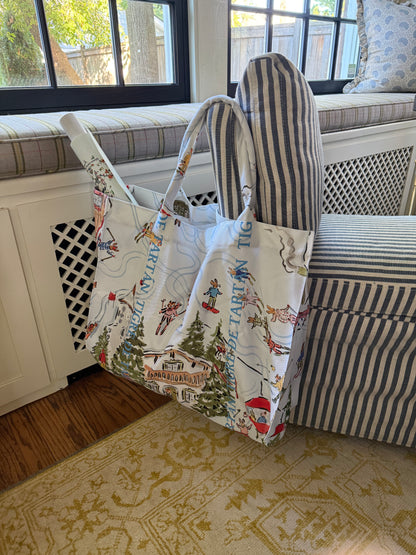 Après Mahj jumbo slouchy denim tote hanging from a striped window-seat bench in a sunlit room